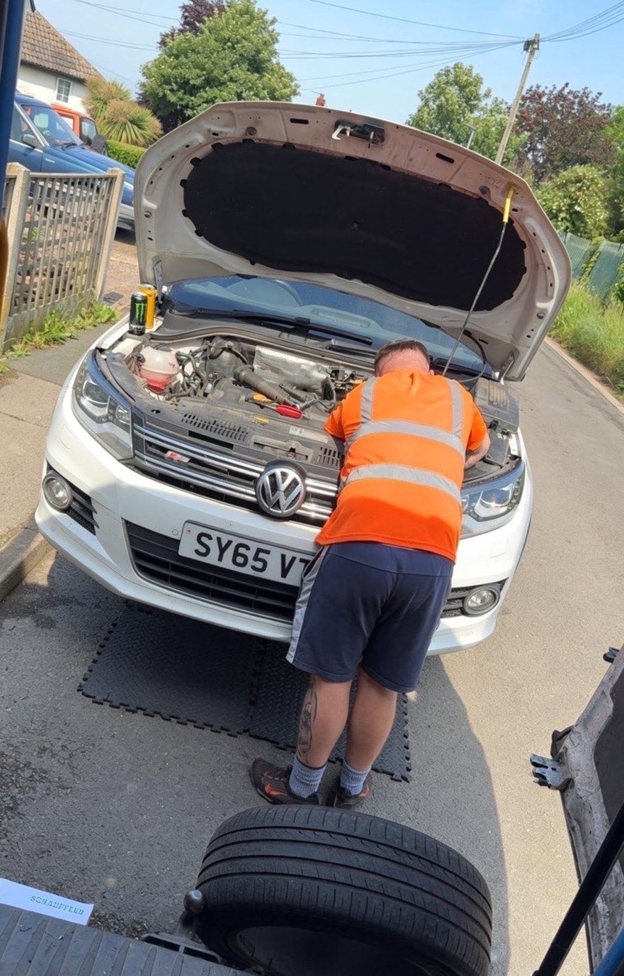 Mechanic in a hi-vis vest working under the bonnet of a van on a customer's driveway