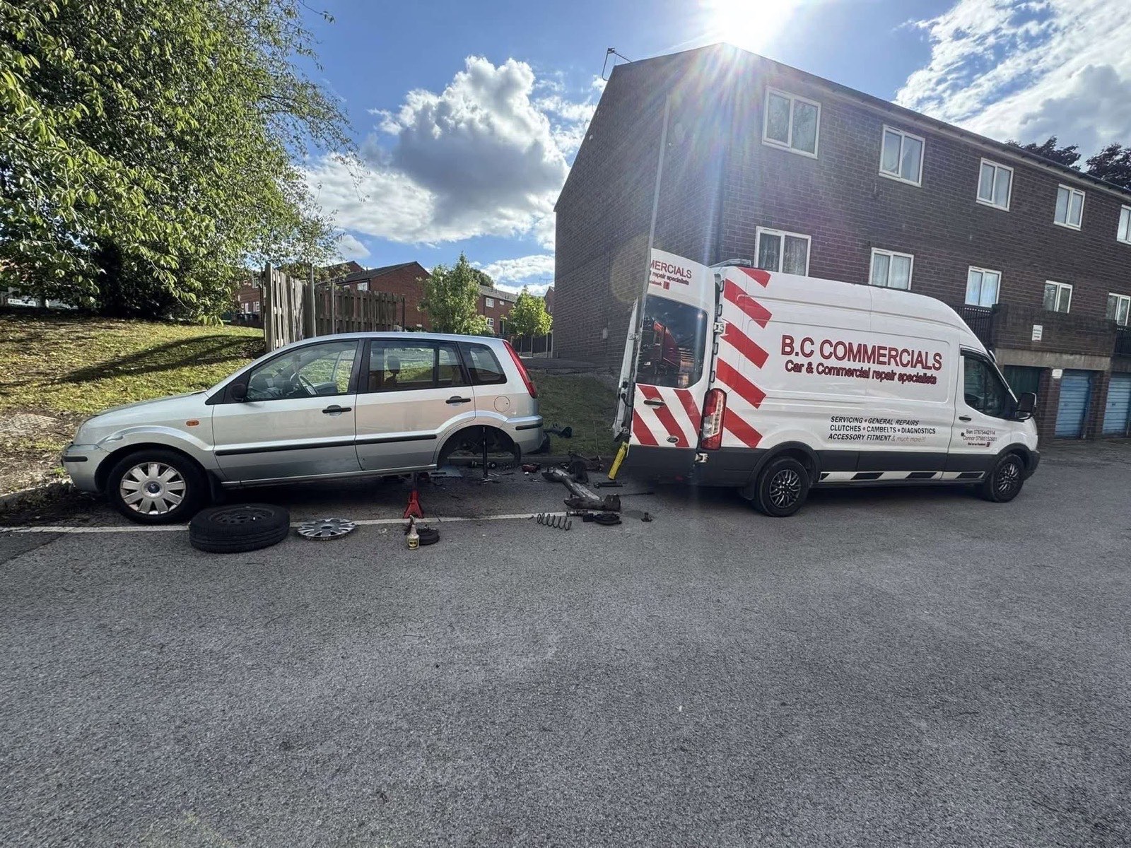 Mechanic replacing suspension components on a car at the kerbside next to the B.C Commercials mobile workshop van